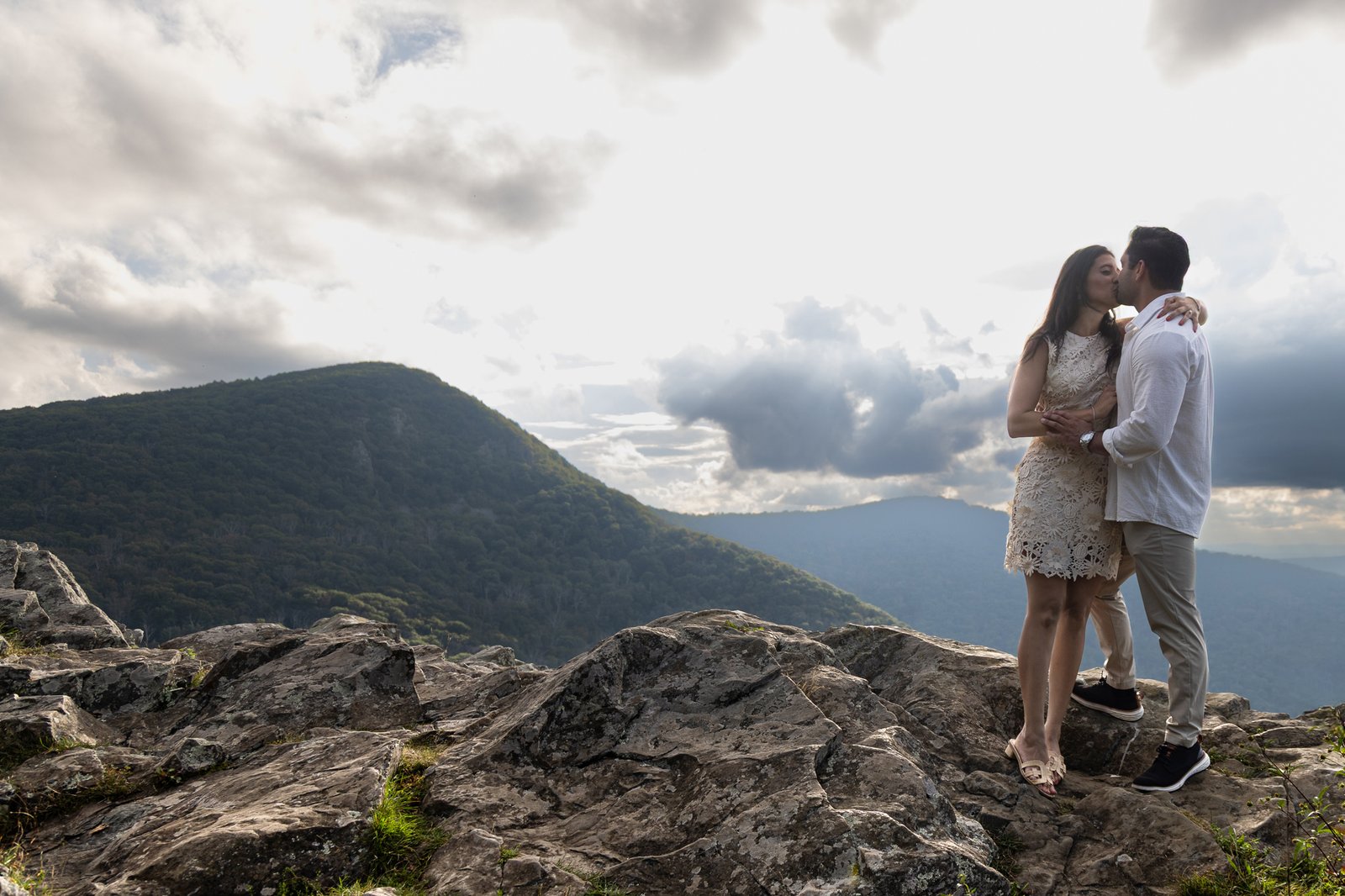 Couple standing on a rock outcrop above layered blue mountains and sun rays in Shenandoah National Park